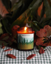 Load image into Gallery viewer, forest candle is lit on a gingham tablecloth